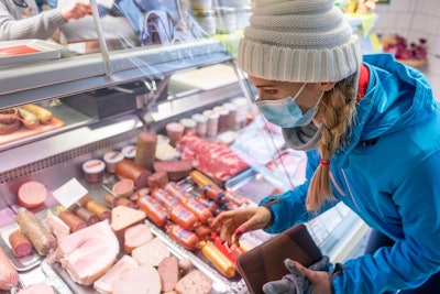 Woman with face mask shopping groceries in covid 19 pandemic at butcher