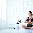 Woman doing yoga. Young beautiful girl in lotus position with her pet at home.