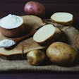 Potato starch with potatoes on a dark wooden background.