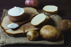Potato starch with potatoes on a dark wooden background.