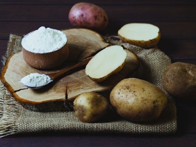 Potato starch with potatoes on a dark wooden background.