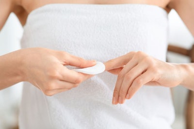 Unrecognizable woman removing lacquer from manicured nails with white cotton pad and acetone. Closeup of lady using nail polisher remover and cotton pad, making manicure at home, cropped