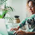 Smart working at home with female and her puppy working on computer together in friendship and love. Cheerful happy woman write on laptop with a dog on her legs. Concept of domestic animals lifestyle