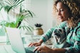 Smart working at home with female and her puppy working on computer together in friendship and love. Cheerful happy woman write on laptop with a dog on her legs. Concept of domestic animals lifestyle
