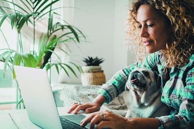 Smart working at home with female and her puppy working on computer together in friendship and love. Cheerful happy woman write on laptop with a dog on her legs. Concept of domestic animals lifestyle