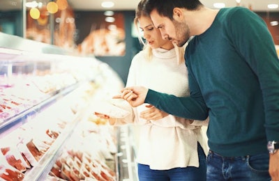 Closeup side view of a late 20's couple choosing some fresh meat for tonight's dinner. They are reading label on one of the packages and seem a bit uncertain about it.