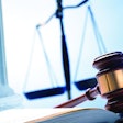 A gavel rests on top of an open law book with a justice scale and a Greek column in the background.