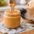 A Peanut Butter Jar With A Bone Shaped Dog Biscuit Dipped Into The Jar A Dog Is Sniffing The Jar