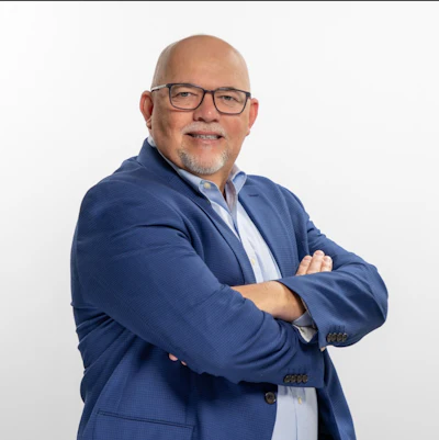 Professional headshot of a middle-aged man wearing glasses and a navy blue blazer with arms crossed