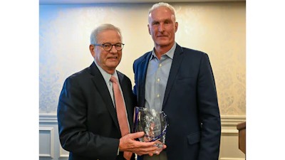 Two professionals pose together at an awards ceremony, one holding a glass trophy
