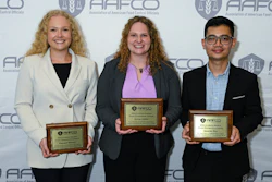 Three professionals holding AAFCO awards at a conference event with branded backdrop