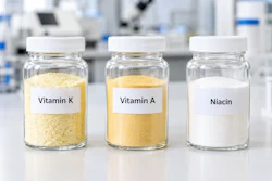 Three glass jars labeled Vitamin K, Vitamin A, and Niacin containing supplement powders in a laboratory setting