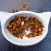 Colorful pet food kibble in a white cat-shaped bowl on a textured blue surface