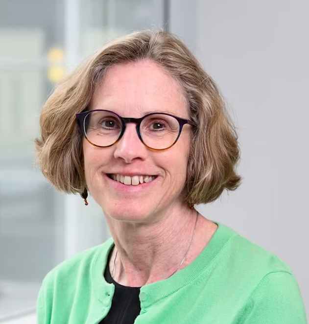 Professional headshot of a smiling woman wearing glasses and a green cardigan over a black top