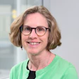Professional headshot of a smiling woman wearing glasses and a green cardigan over a black top
