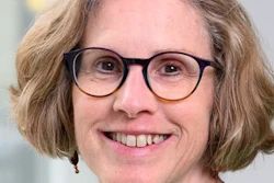 Professional headshot of a smiling woman wearing black-framed glasses with shoulder-length brown hair