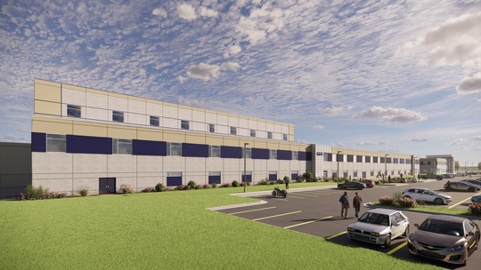 Modern industrial warehouse facility with multi-story design, parking area, and landscaped grounds under cloudy sky