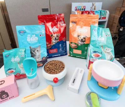 Pet food and accessories display with colorful kibble bags, feeding bowls, and grooming tools on white table