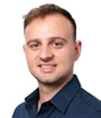 Professional headshot of a smiling man wearing glasses and a dark blue shirt