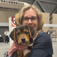 Woman wearing glasses holding a tricolor beagle dog at an indoor event venue