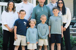 Multi-generational family of nine posing together outdoors in front of a white house with green landscaping