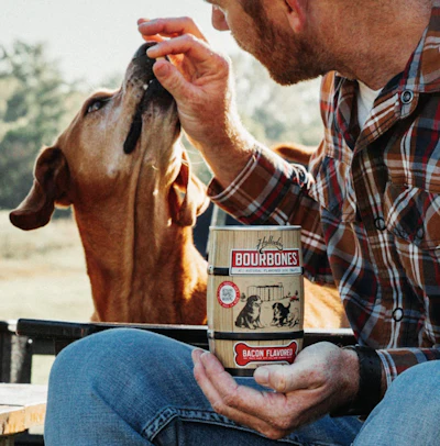 Man feeding dog a Hollings Bourbones bacon-flavored treat outdoors