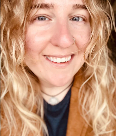 Smiling woman with wavy blonde hair wearing a brown cardigan and nose ring