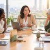 Professional women in business meeting around wooden table with city skyline view in modern office