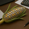 Corn cob filled with coins on desk with laptop, calculator, and pen