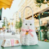White plush cat-shaped gift bag with pink bow and gold heart charm on outdoor café table
