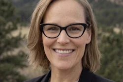 Professional headshot of a smiling woman wearing glasses and dark blazer against a mountainous backdrop