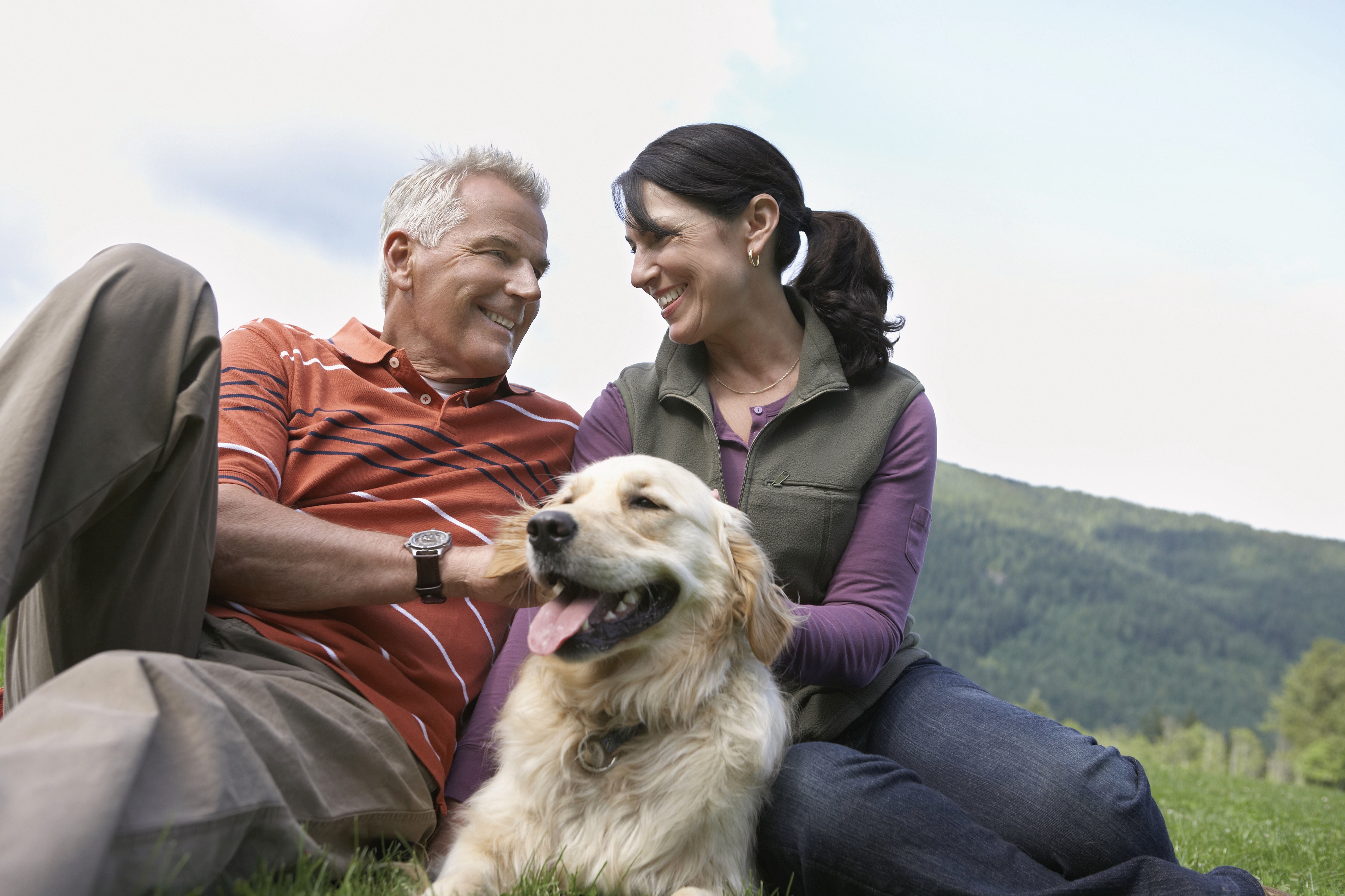 Smiling couple with golden retriever enjoying outdoor time in green hillside landscape