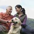 Smiling couple with golden retriever enjoying outdoor time in green hillside landscape