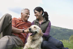 Smiling couple with golden retriever enjoying outdoor time in green hillside landscape