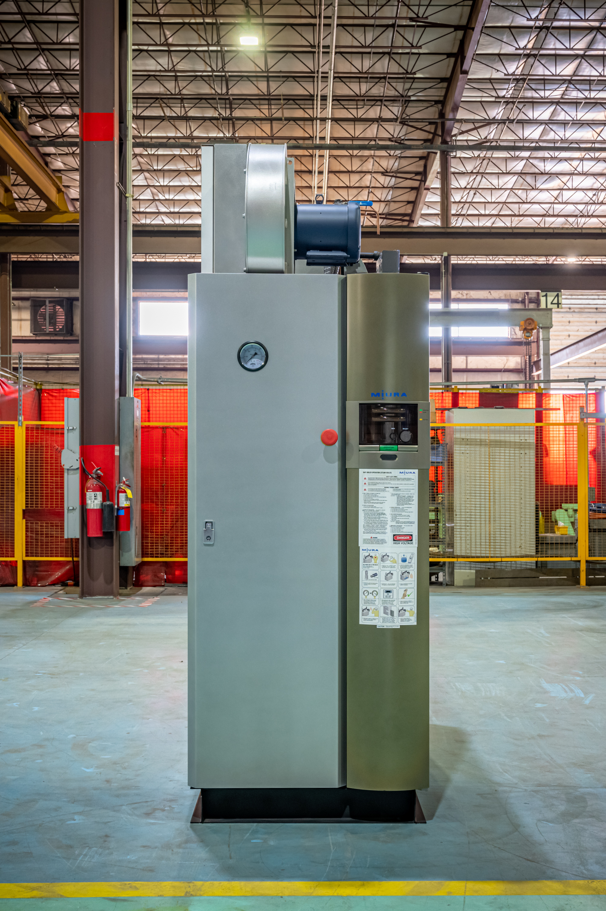 Industrial air compressor system in factory warehouse with red safety barriers and metal framework ceiling