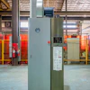 Industrial air compressor system in factory warehouse with red safety barriers and metal framework ceiling