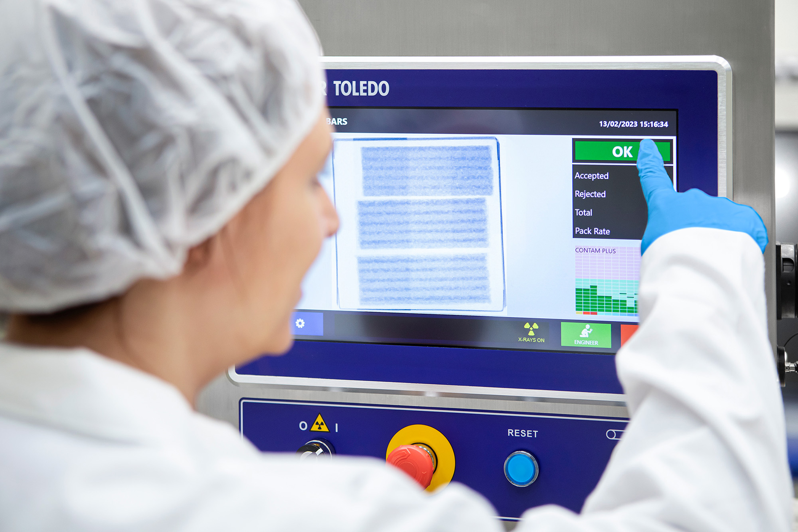 Worker in protective gear operating TOLEDO industrial inspection machine with quality control display showing accepted and rejected items