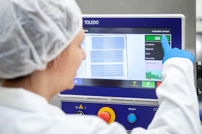 Worker in protective gear operating TOLEDO industrial inspection machine with quality control display showing accepted and rejected items
