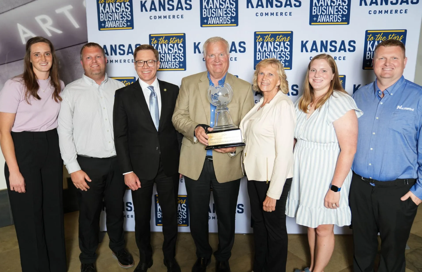 Seven professionals posing with award at Kansas Commerce awards event backdrop