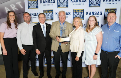 Seven professionals posing with award at Kansas Commerce awards event backdrop