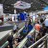 Crowded pet food industry trade show floor with escalators, vendor booths, and branded signage including Petfood Forum banner.