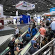 Crowded pet food industry trade show floor with escalators, vendor booths, and branded signage including Petfood Forum banner.
