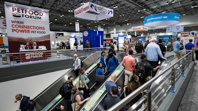 Crowded pet food industry trade show floor with escalators, vendor booths, and branded signage including Petfood Forum banner.