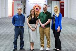 Four Petco employees standing together in store entrance with welcome signage and pet food branding visible behind them