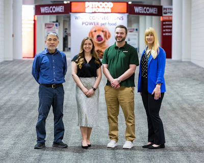 Four Petco employees standing together in store entrance with welcome signage and pet food branding visible behind them