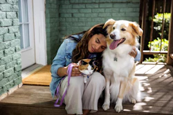 Woman smiling while holding a cat and posing with a golden and white dog on a sunny patio