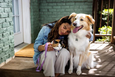 Woman smiling while holding a cat and posing with a golden and white dog on a sunny patio