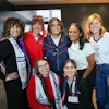Seven women smiling together at an indoor event, some wearing USA team apparel and medals