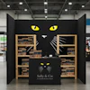Sally & Cie retail booth with black cat face design and wooden shelving displaying products at a trade show