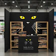 Sally & Cie retail booth with black cat face design and wooden shelving displaying products at a trade show